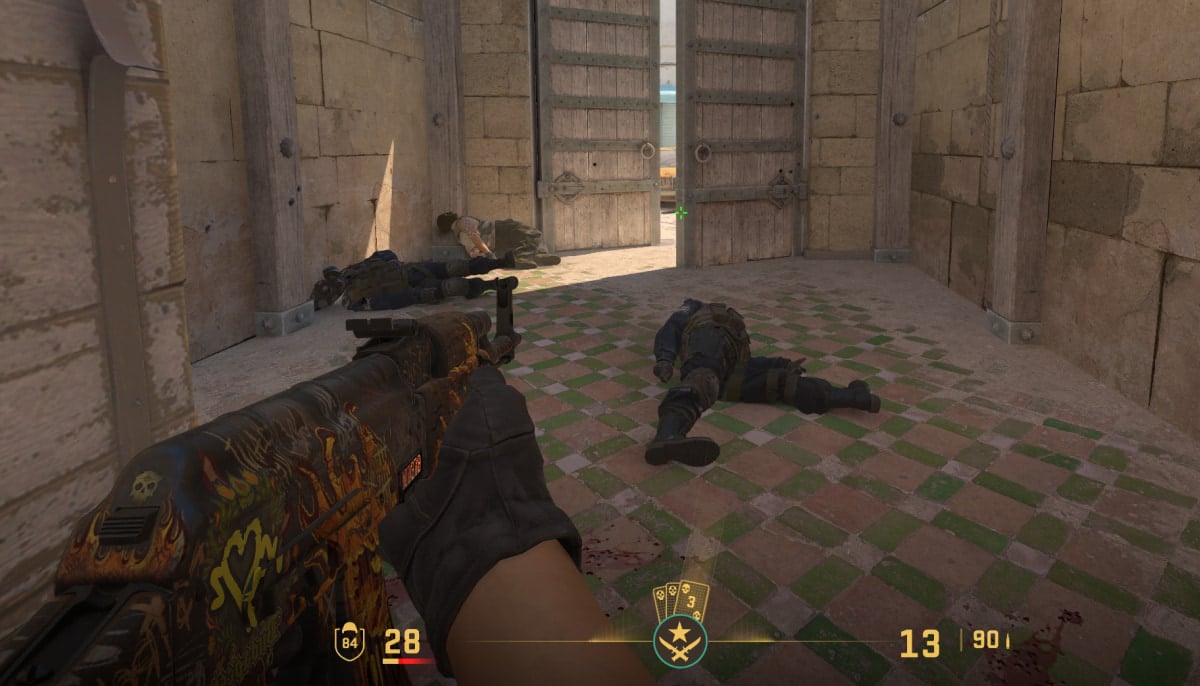 A first-person perspective screenshot from the video game Counter-Strike 2, showing a player's view of a stone courtyard on the map Dust II with several fallen character models on the tiled ground and large wooden doors in the background