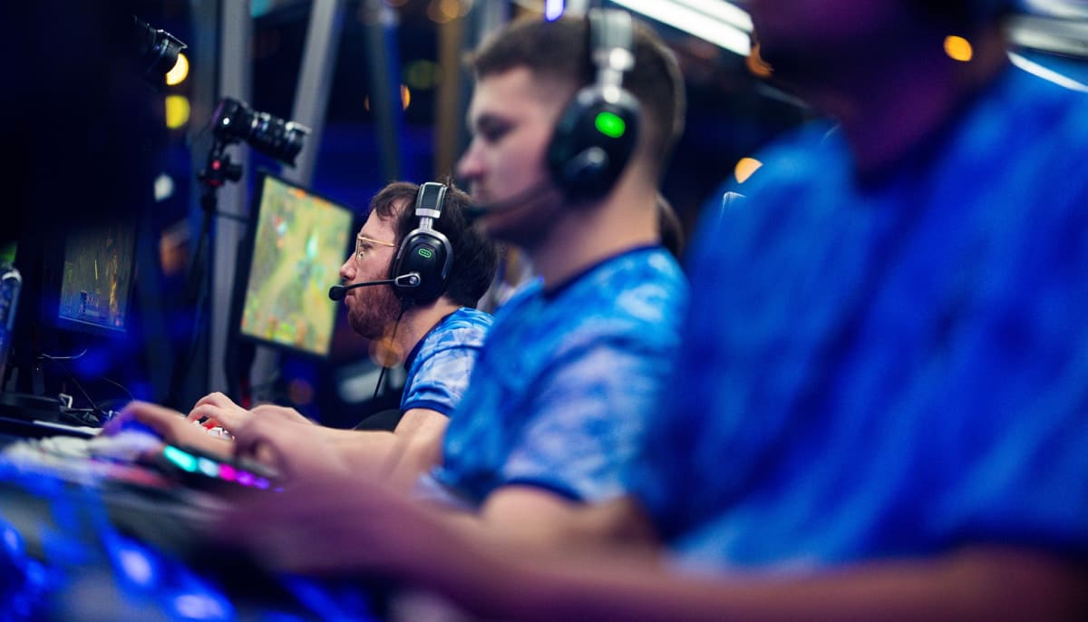 Three professional esports players in blue jerseys and headsets compete during a computer gaming tournament