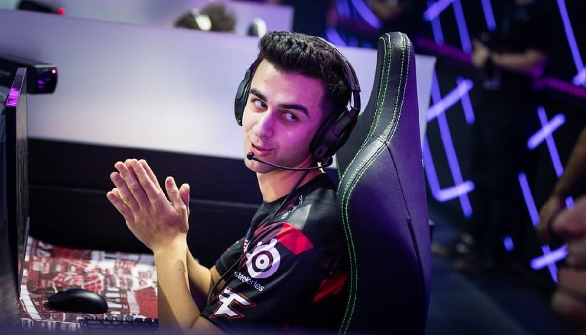 An esports player EpikWhale in a black and red FaZe Clan jersey and a headset looks toward the camera while sitting in a gaming chair at an event