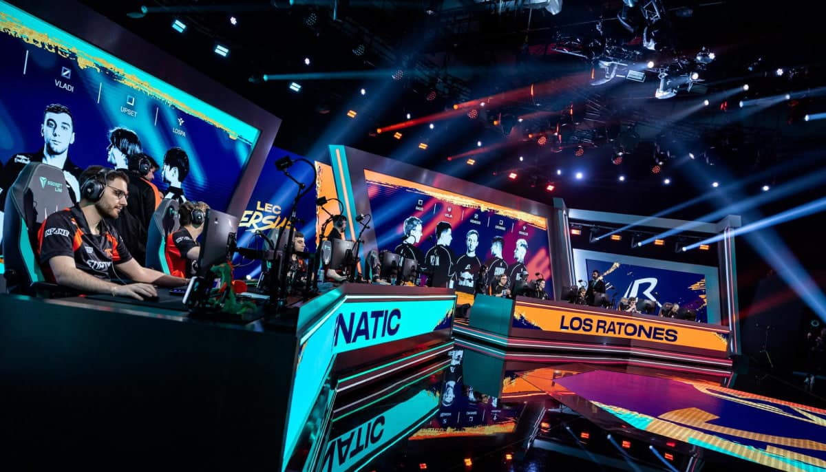 LEC stage at a League of Legends event, featuring G2 Esports (left, with players like Caps and players in black/orange jerseys) versus Fnatic (right, in black jerseys at the "FNATIC" booth) and Los Ratones, with large screens displaying player portraits including Vladi, Upset, and others, under dramatic blue and orange stage lighting with spotlights and a packed audience setup