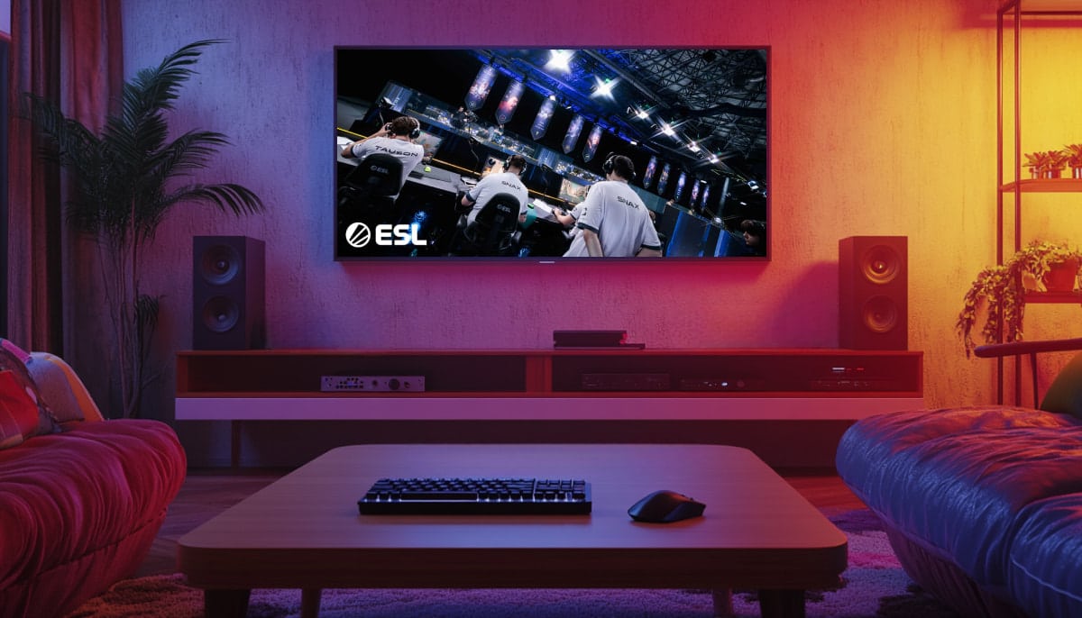 A living room setup with a large TV displaying an ESL (Esports League) Counter-Strike event, featuring professional players on stage, and a keyboard and mouse on the coffee table in the foreground
