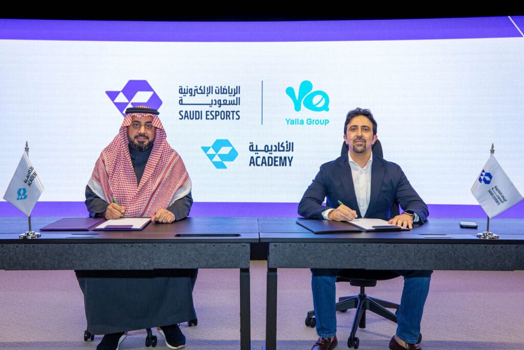 Image of Yalla Group and Saudi Esports Federation representatives signing document while sat at desk