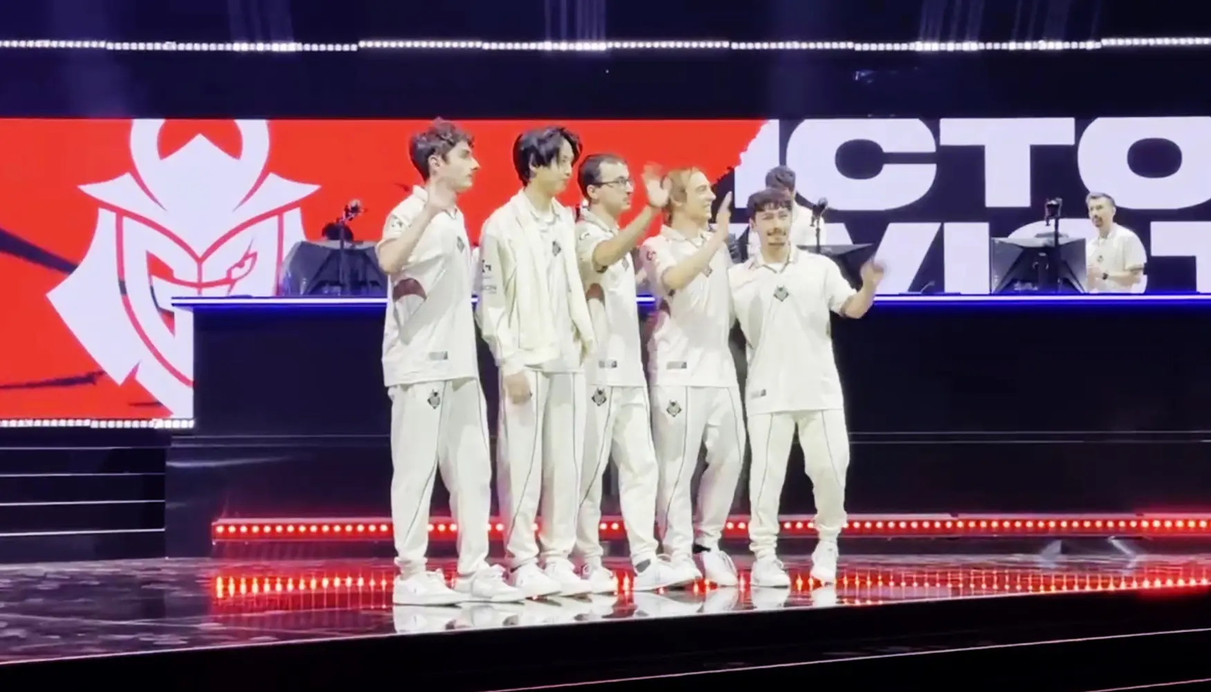 Members of the G2 Esports team standing on a stage in white uniforms in front of a G2 logo.