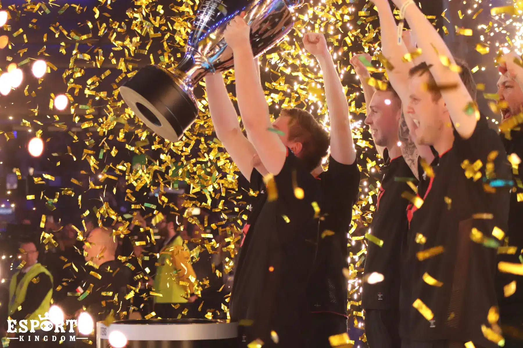 Members of the Astralis esports team celebrate with a trophy amidst falling gold confetti.