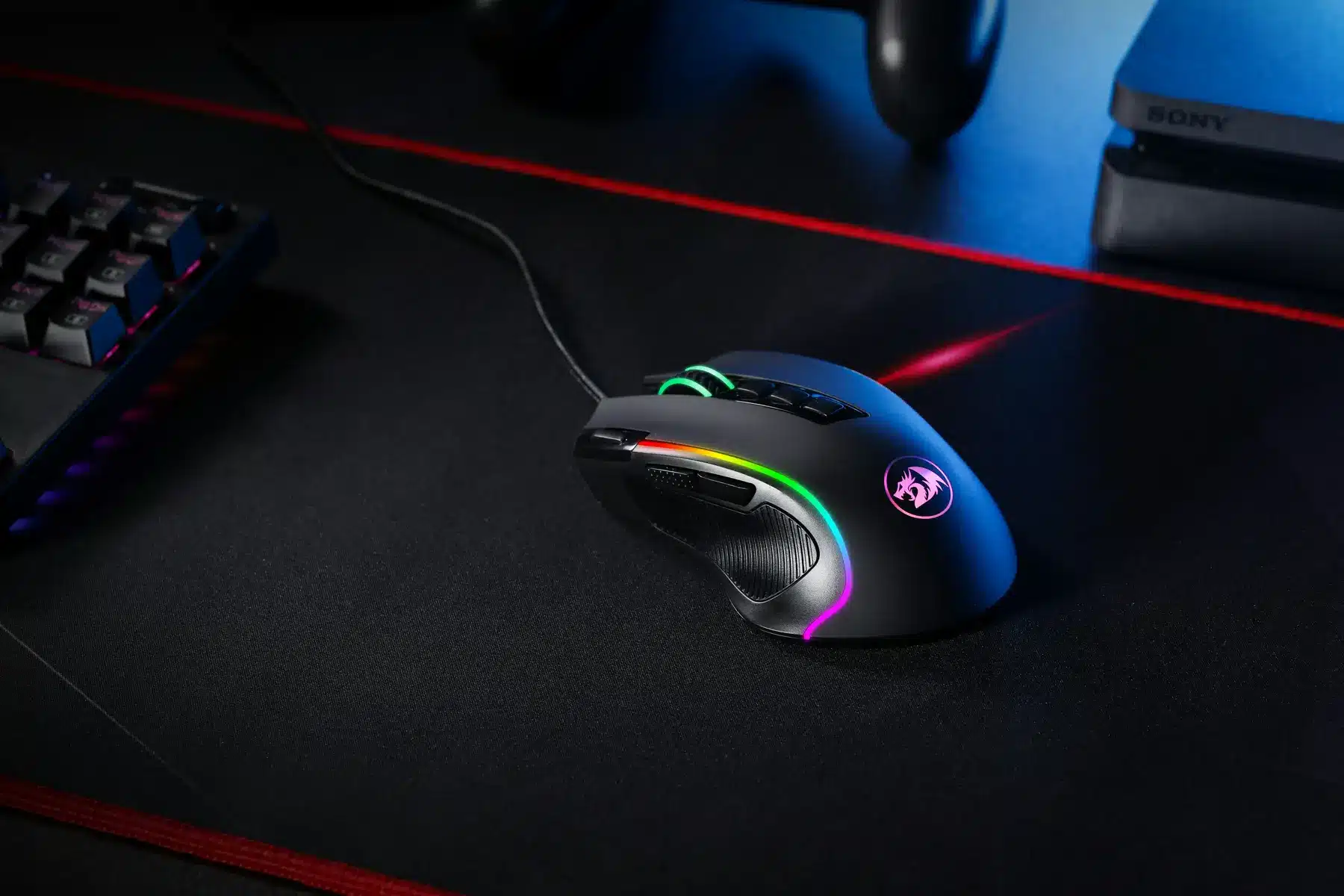 A black gaming mouse with RGB lighting on a black mousepad next to a keyboard